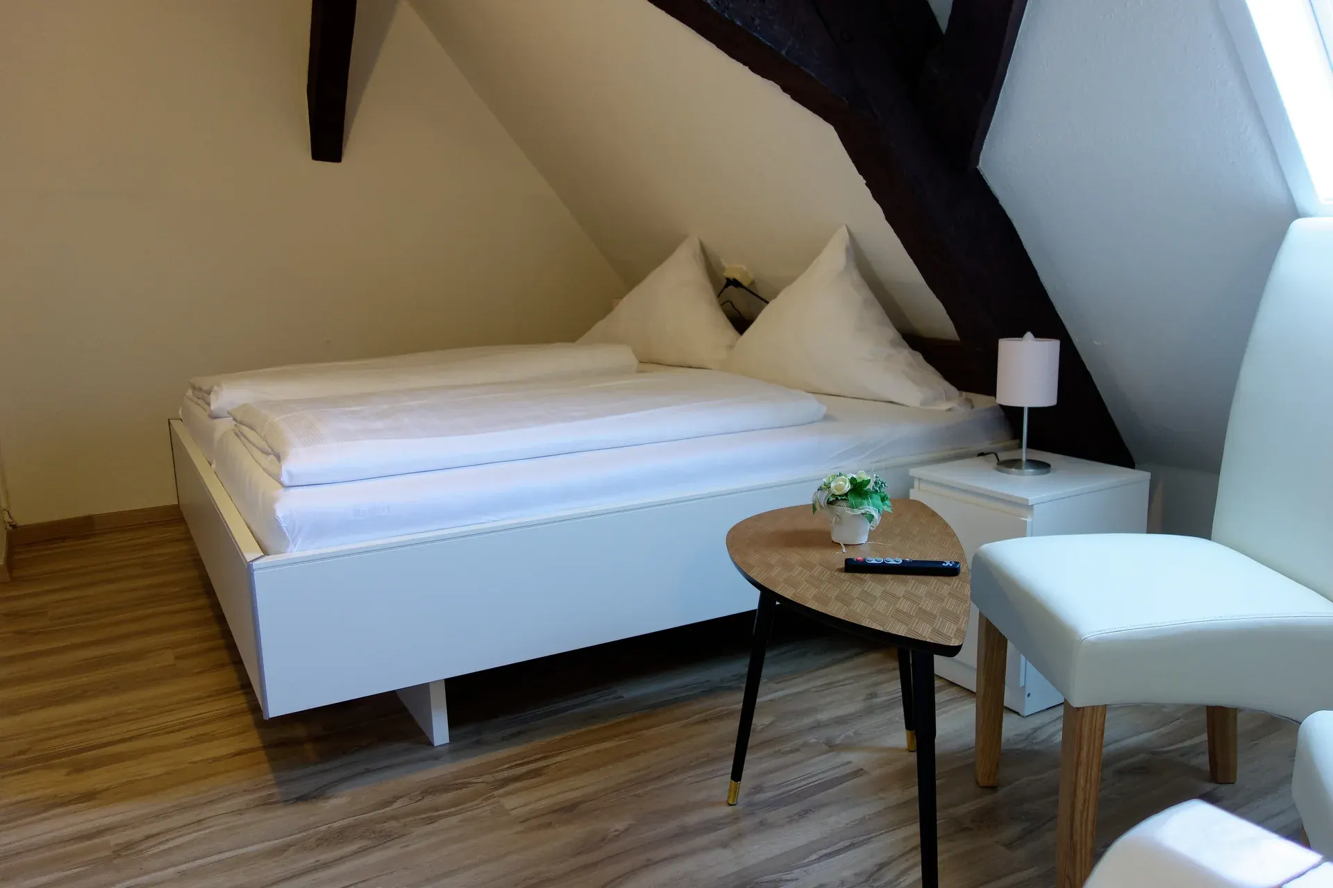 Upper sleeping room of the family accommodation, with white furniture and timber beams