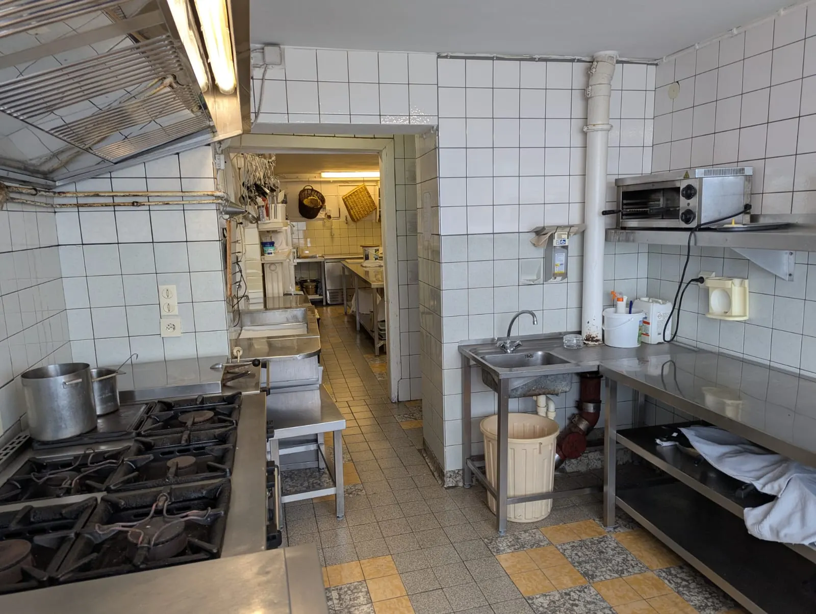 Kochbereich der Gastronomieküche mit Gasherd, Abzugshaube und Edelstahl-Arbeitsflächen