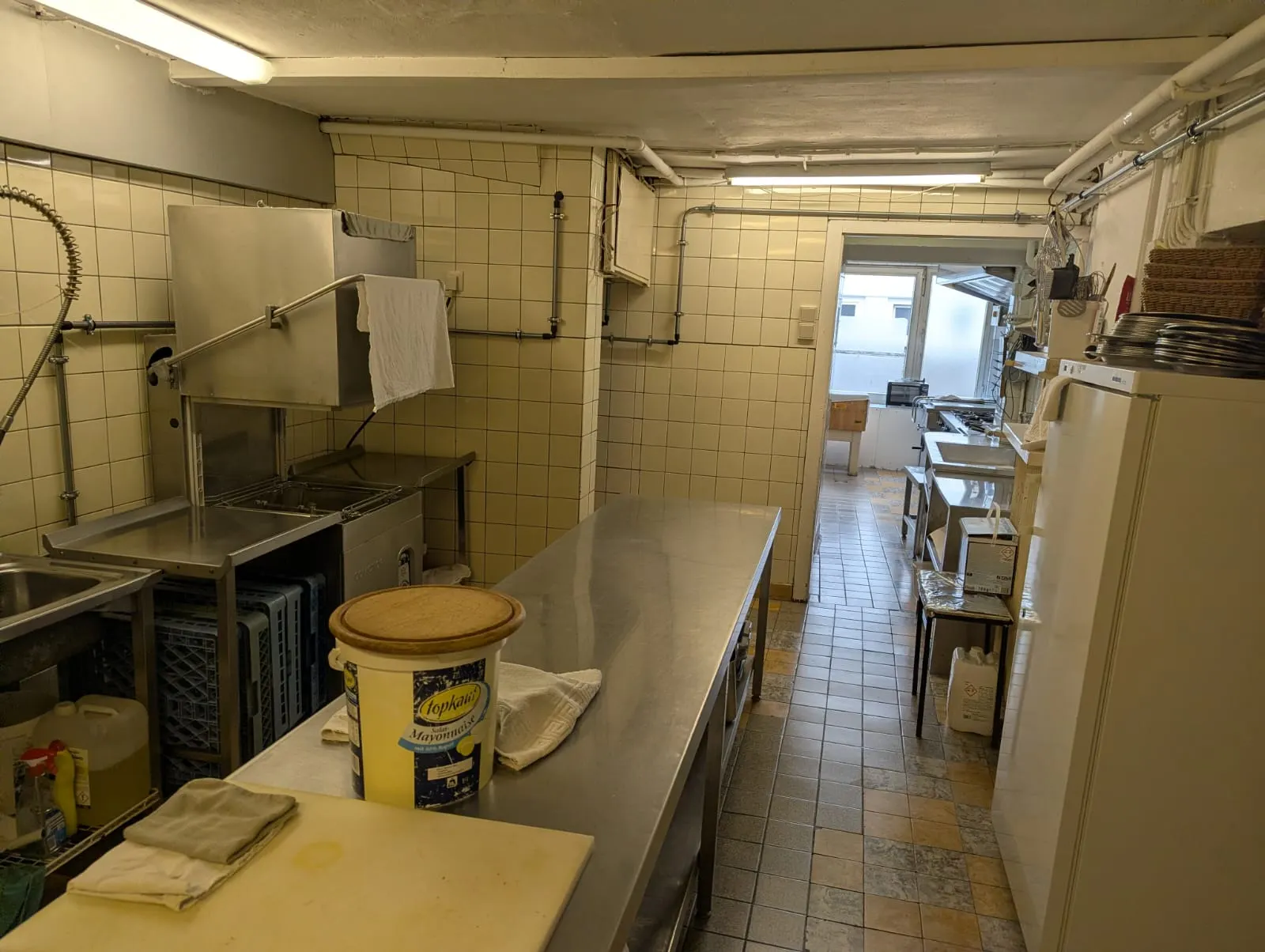 Spül- und Vorbereitungsbereich der Gastronomieküche mit Haubenspülmaschine und Arbeitstischen